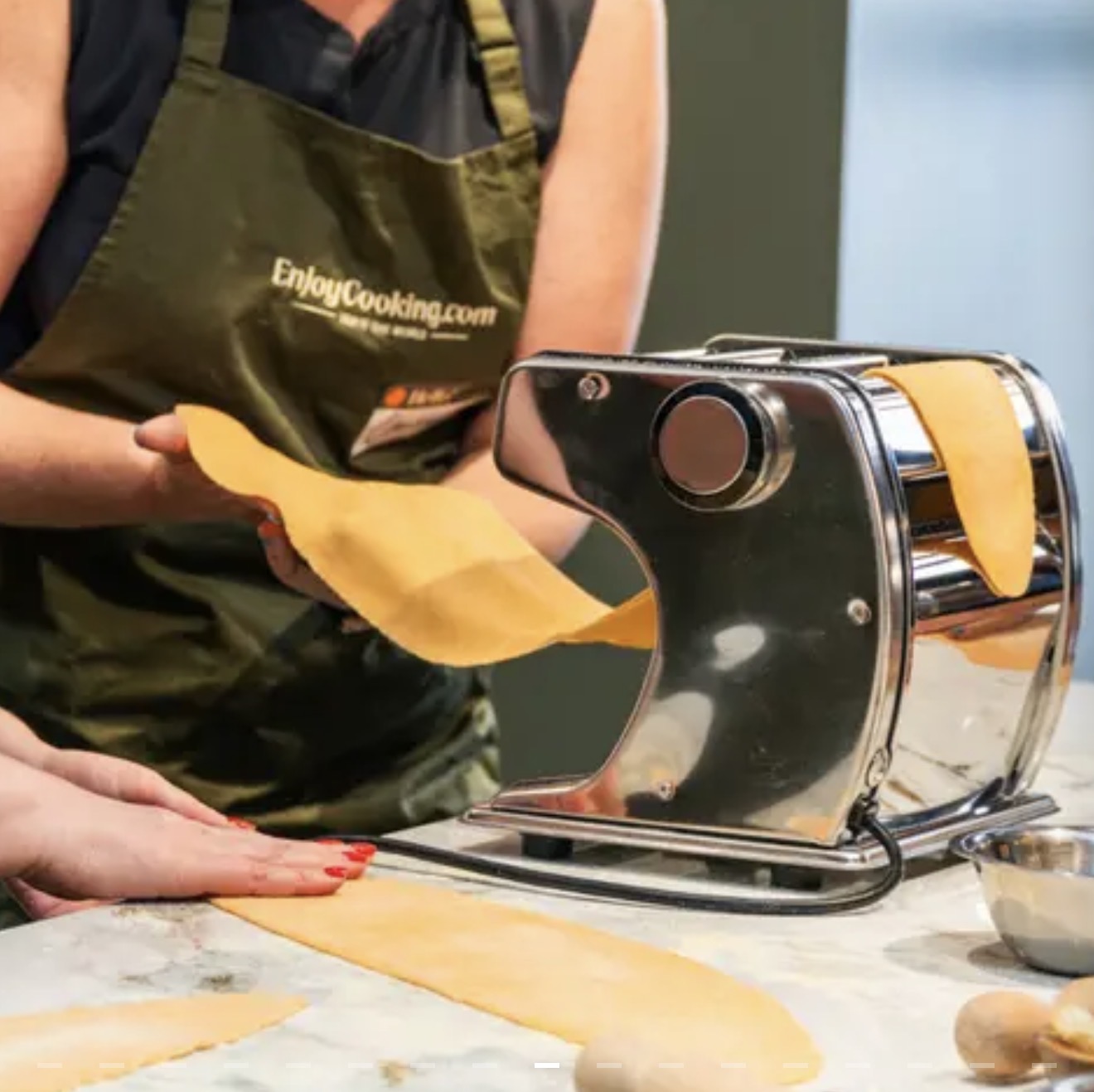 Fresh pasta sheets being rolled through a pasta machine